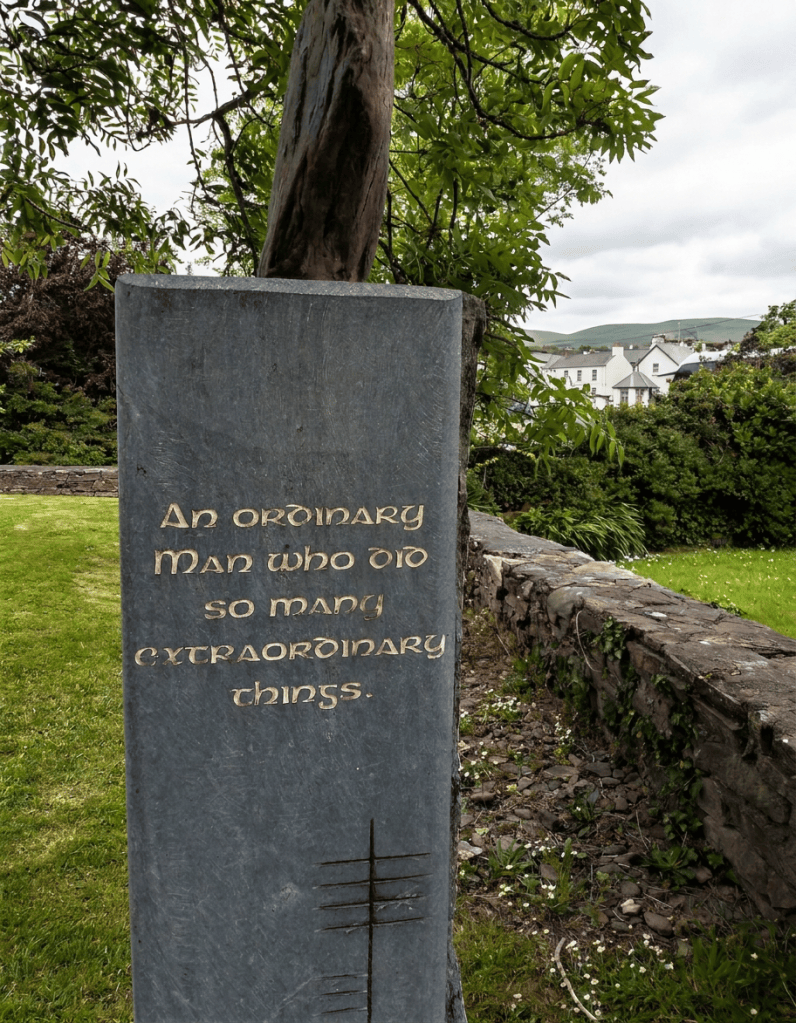 ordinary-man-copy-2 A stone memorial with the inscription 'An ordinary Man who did so many extraordinary things' surrounded by greenery and a low stone wall.